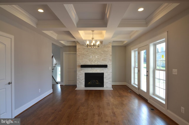 unfurnished living room with a chandelier, coffered ceiling, beam ceiling, a stone fireplace, and dark wood-type flooring