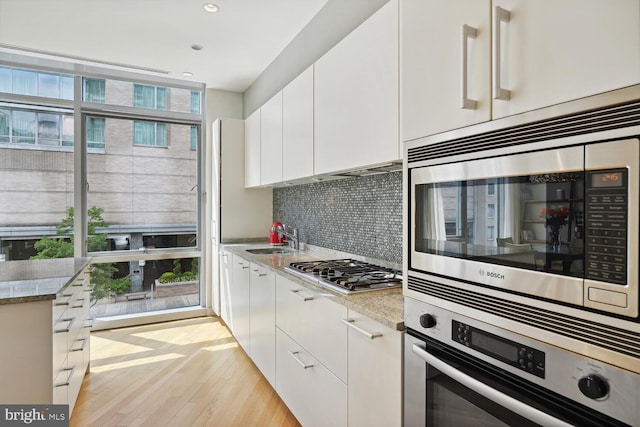 kitchen with white cabinets, stainless steel appliances, light wood-type flooring, and light stone counters