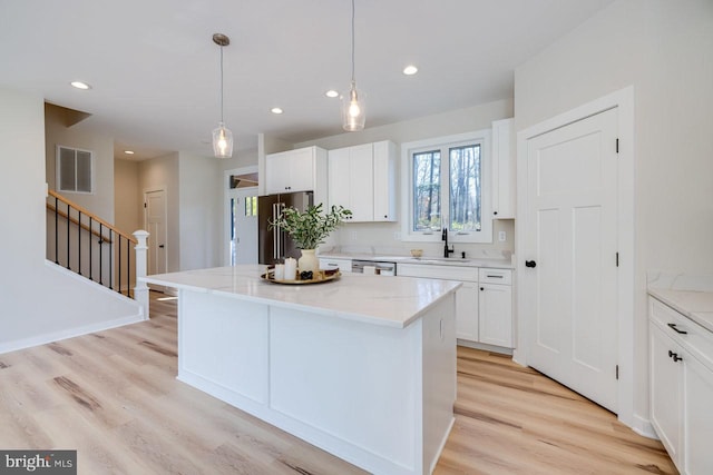 kitchen featuring pendant lighting, white cabinets, appliances with stainless steel finishes, a center island, and light wood-type flooring