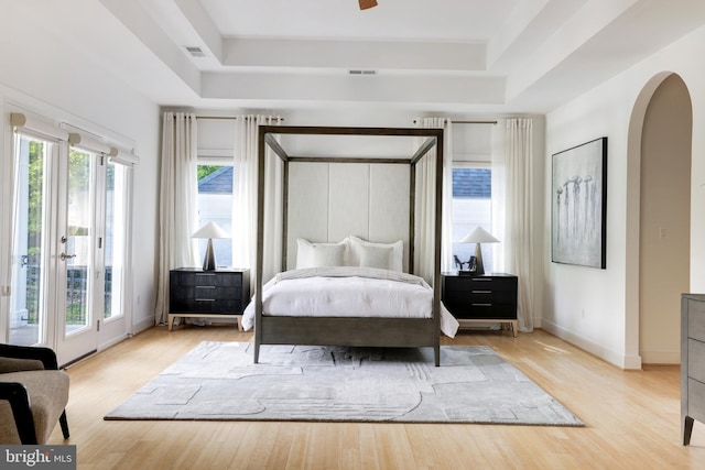 bedroom featuring access to outside, multiple windows, a tray ceiling, and light hardwood / wood-style flooring