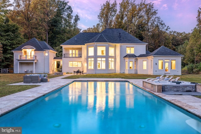 pool at dusk with a yard, an outdoor kitchen, a jacuzzi, and a patio