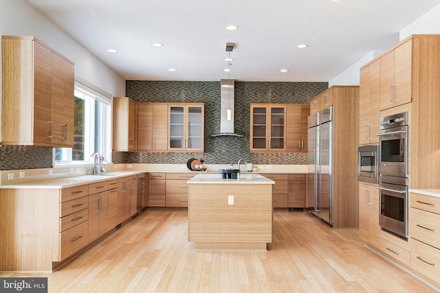 kitchen with backsplash, light hardwood / wood-style floors, stainless steel appliances, an island with sink, and wall chimney exhaust hood