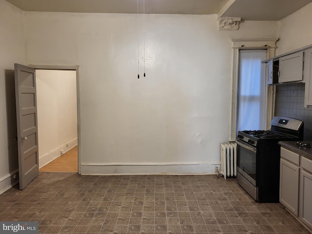 kitchen with dark tile floors, radiator, gray cabinets, and stainless steel gas range oven