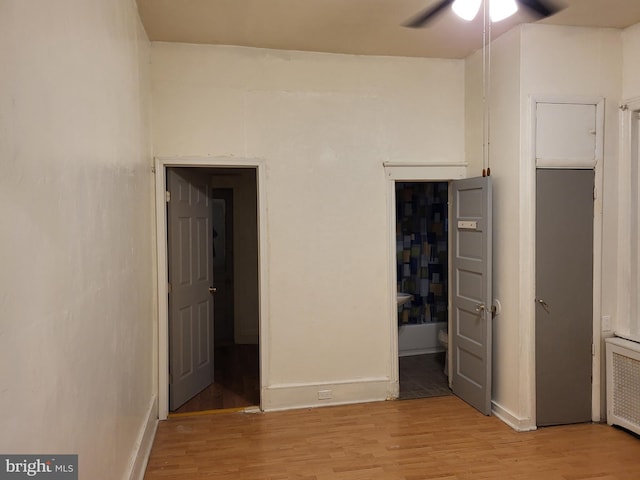 unfurnished bedroom featuring ceiling fan, light hardwood / wood-style flooring, ensuite bathroom, and radiator heating unit