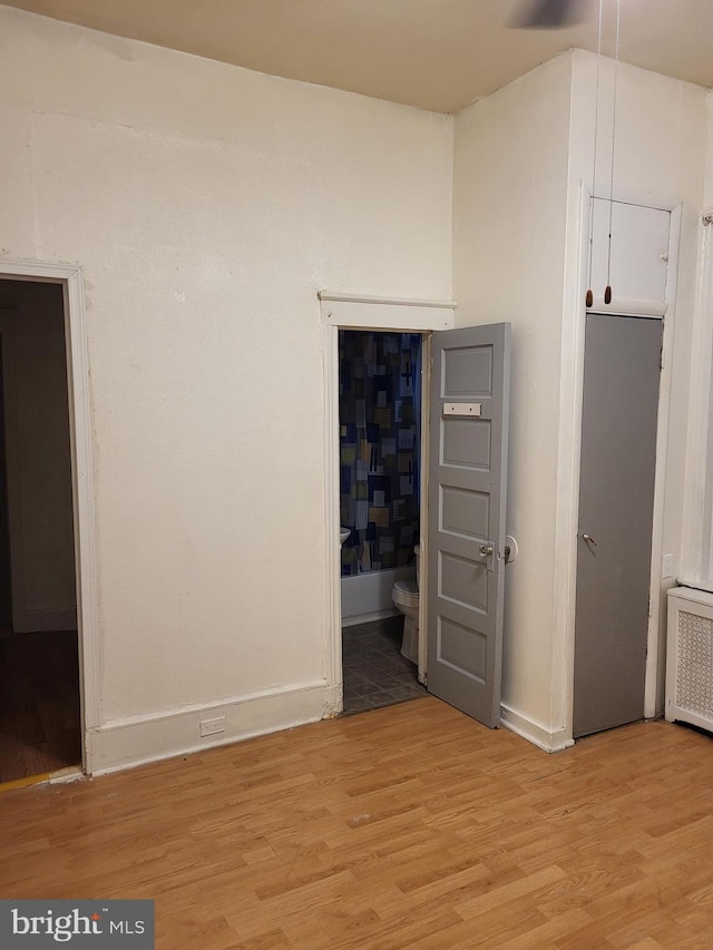 unfurnished bedroom featuring light hardwood / wood-style flooring, ensuite bathroom, and radiator