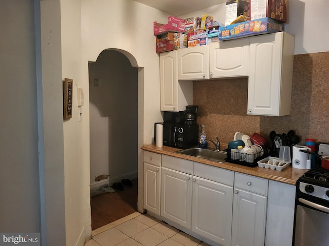 kitchen featuring white cabinetry, stainless steel gas range oven, light tile flooring, sink, and tasteful backsplash