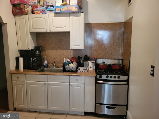 kitchen featuring white cabinets, light tile floors, range with gas cooktop, backsplash, and sink