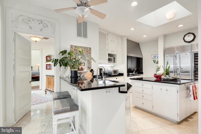 kitchen with dark countertops, visible vents, built in refrigerator, light tile patterned floors, and a peninsula