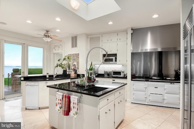 kitchen featuring visible vents, stainless steel microwave, a kitchen island, white cabinets, and a sink