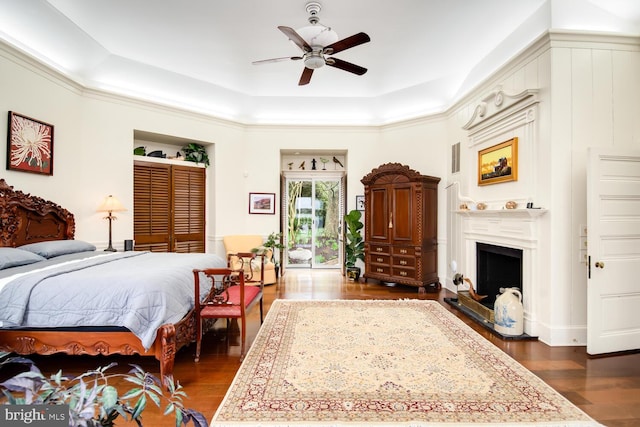 bedroom featuring a fireplace with raised hearth, a ceiling fan, a raised ceiling, and dark wood-type flooring