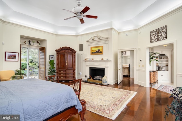 bedroom with wood finished floors, visible vents, a tray ceiling, a fireplace with raised hearth, and access to outside