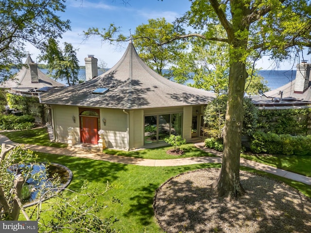 exterior space with roof with shingles, a chimney, and a front lawn