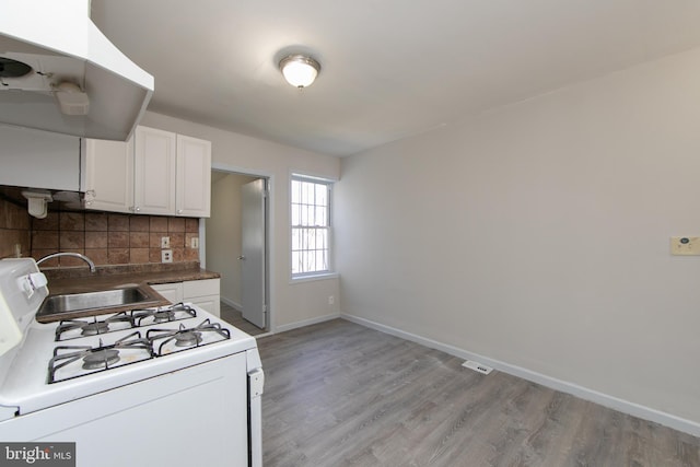 kitchen featuring white cabinetry, tasteful backsplash, white gas stove, and light hardwood / wood-style flooring