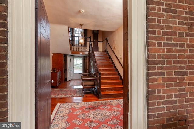 staircase featuring brick wall and hardwood / wood-style flooring