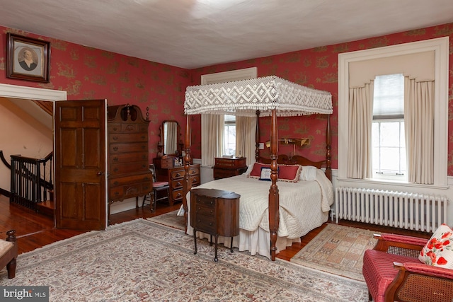 bedroom with wood-type flooring, radiator heating unit, and multiple windows