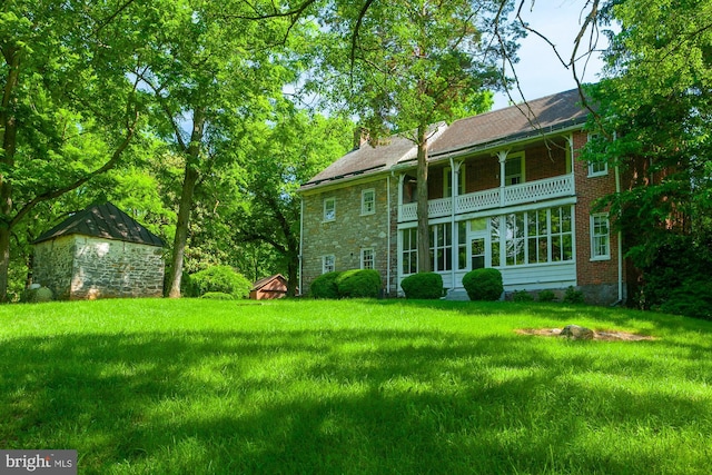 rear view of house with a lawn, a balcony, and a shed