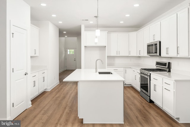 kitchen with a kitchen island with sink, sink, hanging light fixtures, light hardwood / wood-style flooring, and appliances with stainless steel finishes