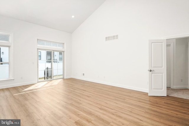 empty room with high vaulted ceiling and light hardwood / wood-style flooring