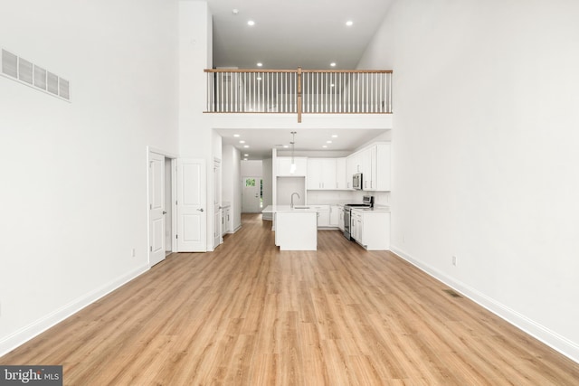 unfurnished living room featuring sink, light wood-type flooring, and a high ceiling