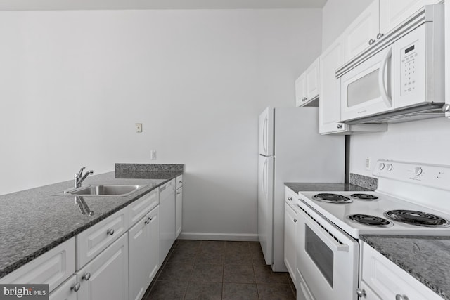 kitchen featuring white cabinets, dark tile flooring, dark stone countertops, white appliances, and sink