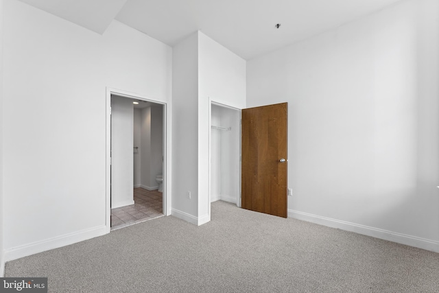 unfurnished bedroom with light carpet, ensuite bath, and a towering ceiling