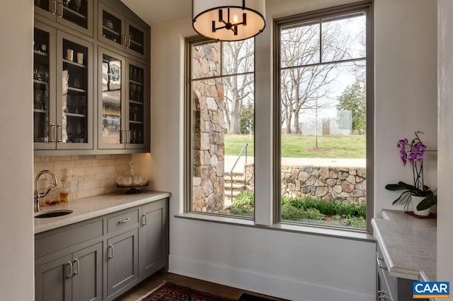 bar featuring a wealth of natural light, gray cabinetry, pendant lighting, and sink