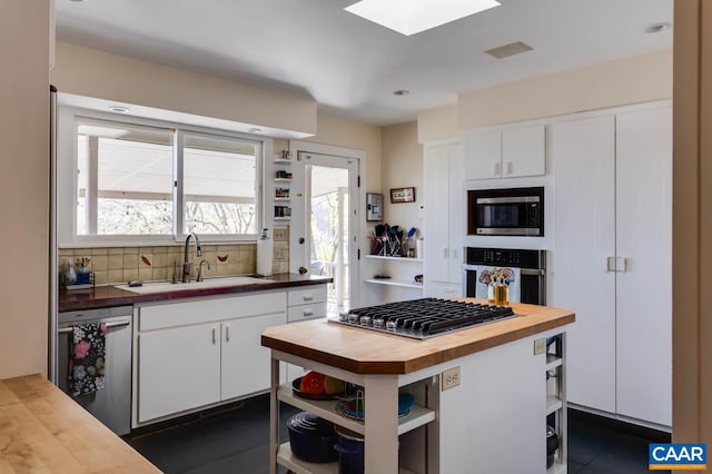 kitchen with appliances with stainless steel finishes, butcher block countertops, tasteful backsplash, white cabinets, and a wealth of natural light