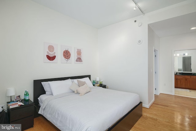 bedroom with rail lighting, light hardwood / wood-style flooring, and ensuite bath