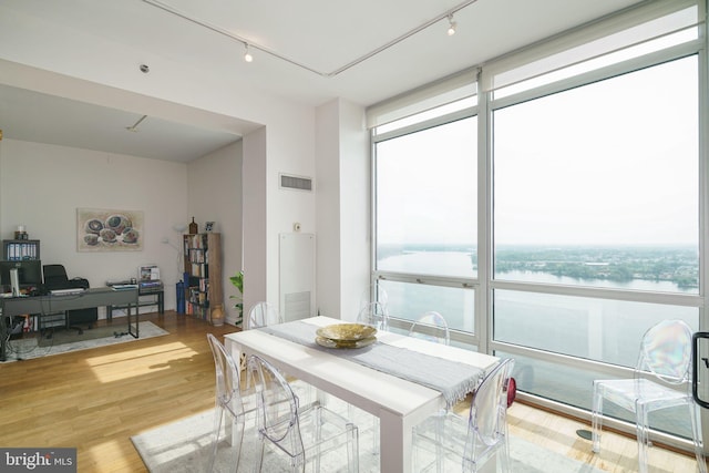 dining space with rail lighting, a water view, floor to ceiling windows, and light hardwood / wood-style floors