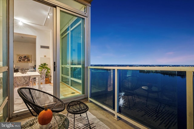 balcony at dusk featuring a water view