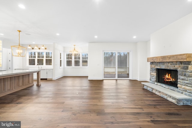 unfurnished living room featuring sink, a stone fireplace, a chandelier, and hardwood / wood-style flooring