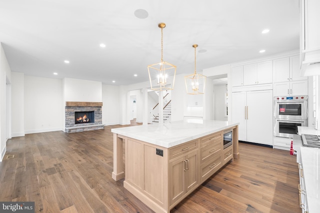 kitchen featuring a kitchen island, built in appliances, hardwood / wood-style floors, pendant lighting, and light stone countertops