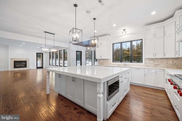 kitchen featuring dark wood-type flooring, tasteful backsplash, a stone fireplace, pendant lighting, and stainless steel microwave