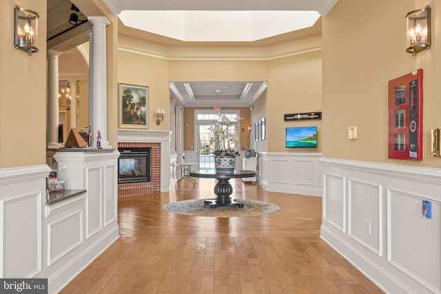 entrance foyer with crown molding, decorative columns, a raised ceiling, and a brick fireplace