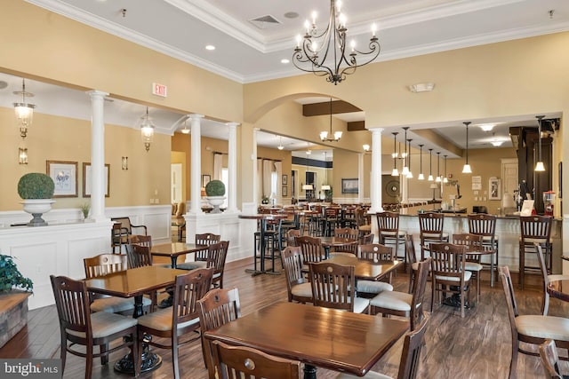 dining area featuring an inviting chandelier, a high ceiling, dark wood-type flooring, a tray ceiling, and ornate columns