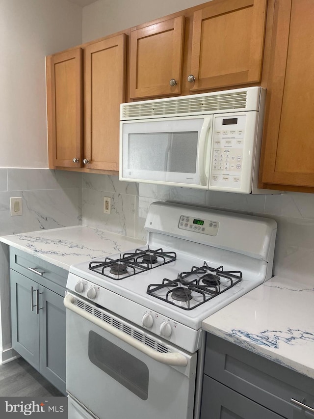 kitchen featuring white appliances, light stone countertops, tasteful backsplash, and gray cabinetry