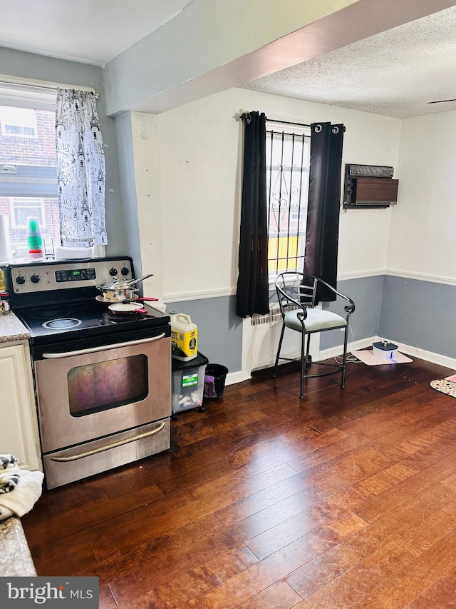 kitchen with dark hardwood / wood-style flooring, an AC wall unit, stainless steel range with electric cooktop, and a textured ceiling