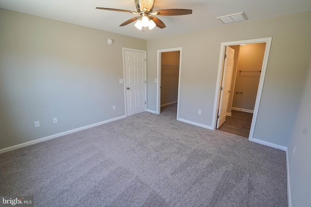 unfurnished bedroom featuring ceiling fan, a spacious closet, a closet, connected bathroom, and carpet floors