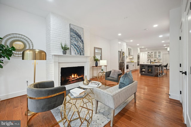 living room with brick wall, hardwood / wood-style floors, sink, and a brick fireplace