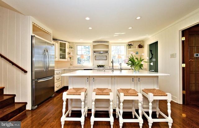 kitchen with white cabinets, a breakfast bar area, dark hardwood / wood-style floors, an island with sink, and stainless steel fridge