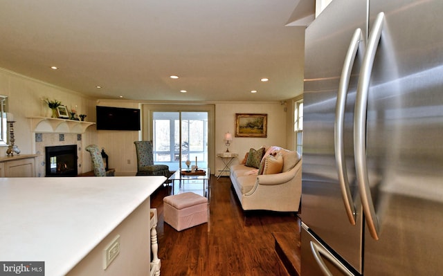 kitchen with stainless steel refrigerator, dark wood-type flooring, a tiled fireplace, white cabinetry, and ornamental molding