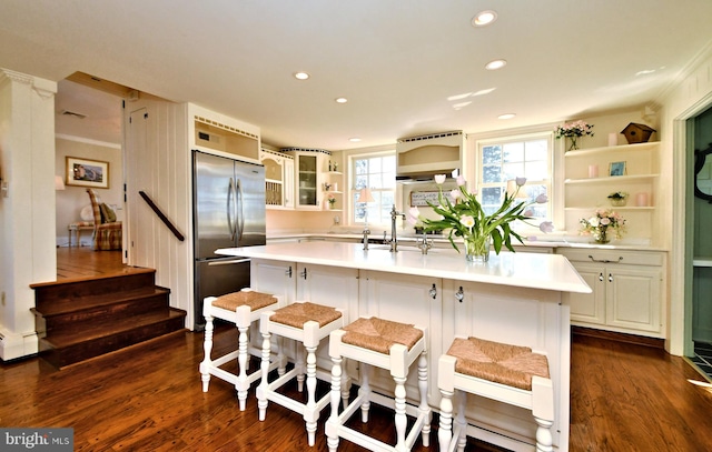 kitchen featuring dark hardwood / wood-style flooring, a kitchen breakfast bar, high end refrigerator, a kitchen island with sink, and white cabinets