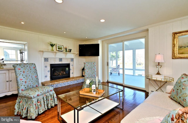 living room with dark hardwood / wood-style flooring, a tiled fireplace, and crown molding