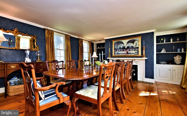 dining room featuring a fireplace, ornamental molding, built in shelves, and hardwood / wood-style floors