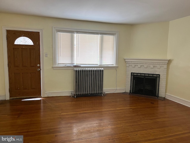 foyer entrance with dark hardwood / wood-style floors, radiator, and a brick fireplace