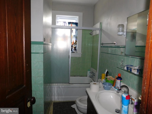 full bathroom with tile walls, toilet, enclosed tub / shower combo, and vanity