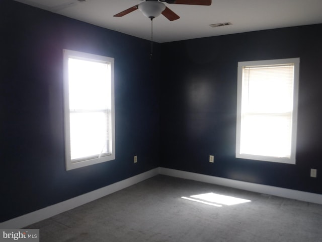 empty room featuring plenty of natural light, ceiling fan, and dark carpet