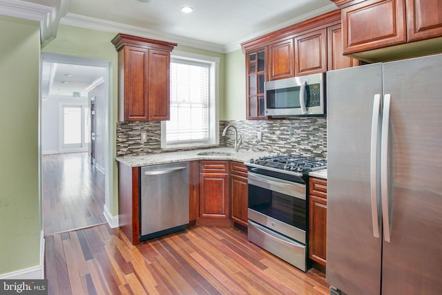 kitchen featuring light stone countertops, light wood-type flooring, backsplash, stainless steel appliances, and sink