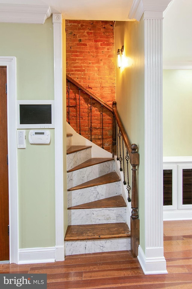 stairs with ornate columns, hardwood / wood-style floors, and crown molding