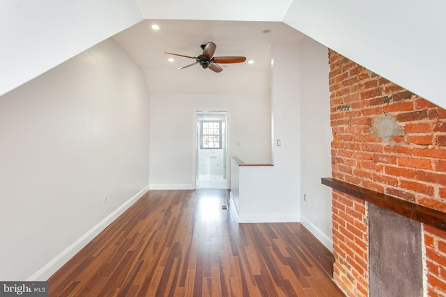 unfurnished living room with ceiling fan, a fireplace, lofted ceiling, brick wall, and dark hardwood / wood-style flooring